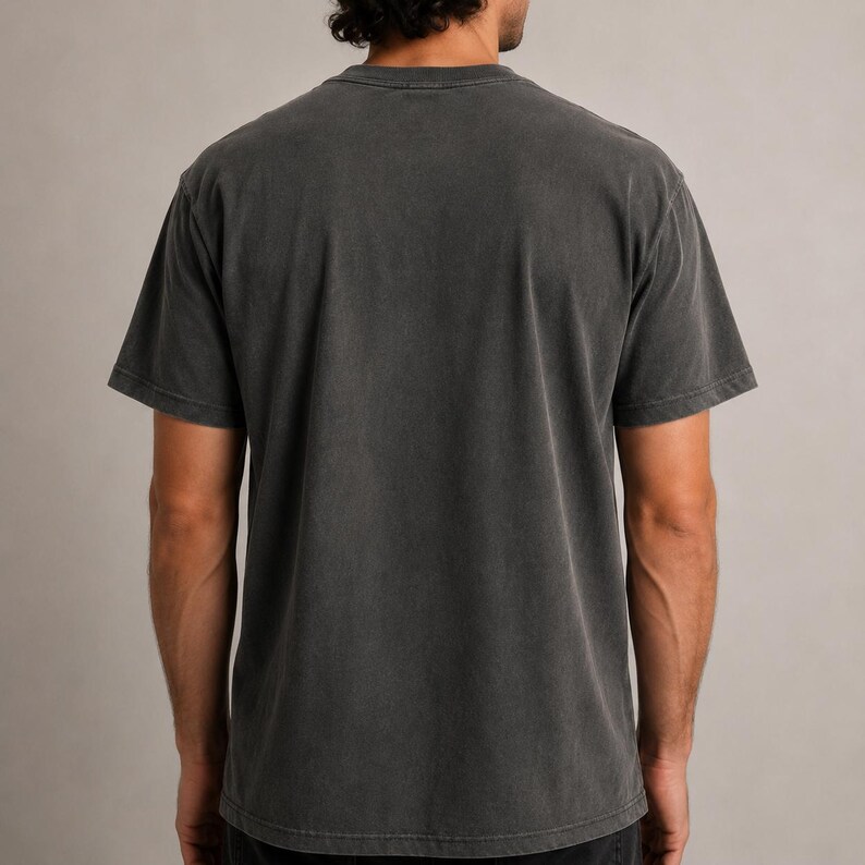 K&ouml;nnte beinhalten: Ein anthrazitfarbenes, kurz&auml;rmeliges T-Shirt. Das Shirt hat einen Rundhalsausschnitt und ein leicht verwaschenes Aussehen. Die R&uuml;ckseite des Shirts ist sichtbar und zeigt die Schultern und den oberen R&uuml;cken. Der Stoff scheint eine weiche Baumwollmischung zu sein.