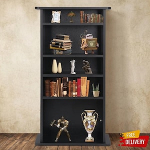 May include: A tall black bookshelf with five shelves containing various items including books, a small picture frame, a lamp, a wooden robot figure, two white vases, a white statue, a bronze statue, a small plant, a warrior figure, and a decorative vase.