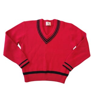 May include: A bright red long-sleeve V-neck sweater featuring dark navy blue striped detailing along the neckline, cuffs, and hem. The garment includes a white interior brand label at the neck with the text Champion visible on the tag.