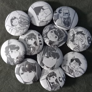May include: A selection of black and white manga-style badges. Each badge displays a different panel from a comic, featuring characters and expressions. The badges are circular and have a shiny finish.