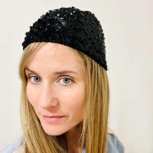 May include: A black sequin beret. The hat is made of small, shiny, black sequins and is worn on the head. The beret is a classic style, perfect for adding a touch of glamour to any outfit.