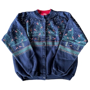 May include: Navy blue button-up sweatshirt with a red collar. The sweatshirt features a winter scene with green Christmas trees, red birds, and white snowflakes. The sleeves and bottom hem have a teal and pink patterned border.