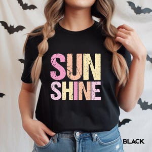 Black t-shirt with 'SUNSHINE' graphic in distressed lettering in pink, orange, and yellow