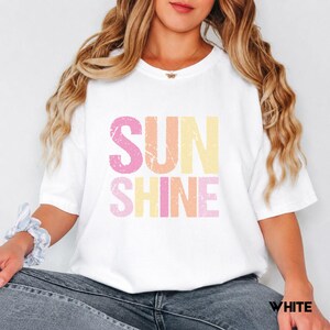 White t-shirt with 'SUNSHINE' graphic in distressed pink, orange, and yellow lettering