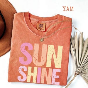 Coral comfort colors t-shirt with 'SUNSHINE' graphic in pink and yellow gradient, Comfort Colors tag