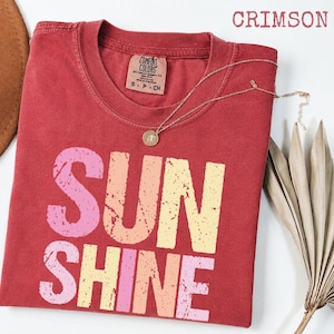 Crimson t-shirt with 'SUNSHINE' graphic in pink, orange, and yellow gradient lettering