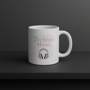 Könnte beinhalten: Weiße Keramiktasse mit dem Text "Techno-Mausi" in rosa-violetter Schrift und einer schwarz-weißen Kopfhörergrafik. Die Tasse steht auf einer schwarzen Oberfläche vor einem dunkelgrauen Hintergrund.