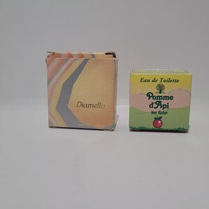 Op de afbeelding: Twee vintage parfumdozen. De eerste is een vierkante doos met een geometrisch ontwerp en de naam "Diamella". De tweede doos is gemarkeerd met "Pomme d'Api" met een appel en "Eau de Toilette".