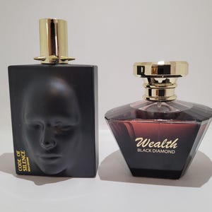 Könnte beinhalten: Zwei Parfümflaschen. Eine ist eine schwarze, rechteckige Flasche mit einem Gesicht auf der Vorderseite und dem Text "CODE OF SILENCE". Die andere ist eine facettierte, dunkelrote Flasche mit "Wealth BLACK DIAMOND" in goldener Schrift.