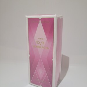 Könnte beinhalten: Eine rosa-weiße rechteckige Schachtel mit dem Text "AVON EVE EMBRACE" in goldfarbenen Buchstaben. Die Schachtel hat ein geometrisches Design in Rosatönen und einen weißen Rand. Die Worte "Limited Edition" stehen oben.