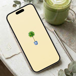 May include: A smartphone with a yellow screen displaying a watercolor illustration of a small tree in a blue and white pot. A cup of green beverage and a pencil are also visible.