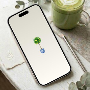 May include: A smartphone displays a watercolor illustration of a small lemon tree in a blue and white pot. A glass of green beverage and a pencil are next to the phone. The phone has a black border and a white screen.