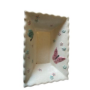 May include: Rectangular off-white ceramic dish with a scalloped edge. The dish is decorated with a pink butterfly, a teal butterfly, and small floral accents in pink and teal.