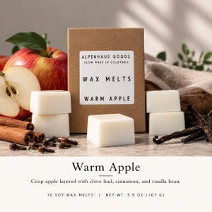 May include: A brown cardboard box of Alpenhaus Goods wax melts labeled Warm Apple, net weight 5.9 oz. The box is surrounded by white wax cubes, a whole red apple, a sliced apple, cinnamon sticks, whole cloves, and vanilla beans.