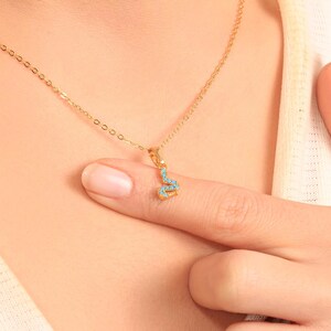 May include: A gold necklace featuring a snake pendant. The pendant is embellished with small, turquoise-coloured stones. The necklace is shown on a person's skin, with the pendant resting on a finger.