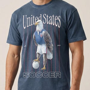 Vintage USMNT soccer fan graphic t-shirt with bald eagle soccer player on a washed navy comfort colors graphic tee of USA world cup soccer fans