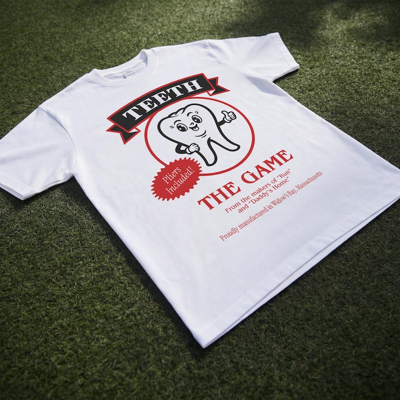 May include: A white short-sleeve t-shirt featuring a graphic of a cartoon tooth with the text TEETH THE GAME, Pliers Included!, From the makers of Run and Daddy's Home, and Proudly manufactured in Widow's Bay, Massachusetts printed in red and black.