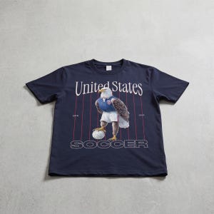 Vintage USMNT soccer fan graphic t-shirt with bald eagle soccer player and pinstripes on a navy graphic tee of USA world cup soccer fans