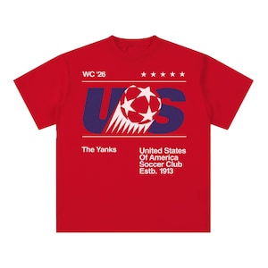 K&ouml;nnte beinhalten: Ein rotes T-Shirt mit einem grafischen Design mit den Buchstaben "US" in Blau, einem Fu&szlig;ball und dem Text "WC '26". Zus&auml;tzlicher Text enth&auml;lt "The Yanks" und "United States Of America Soccer Club Estb. 1913".