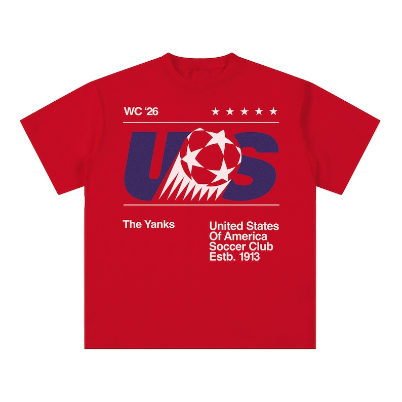 K&ouml;nnte beinhalten: Ein rotes T-Shirt mit einem grafischen Design mit den Buchstaben "US" in Blau, einem Fu&szlig;ball und dem Text "WC '26". Zus&auml;tzlicher Text enth&auml;lt "The Yanks" und "United States Of America Soccer Club Estb. 1913".