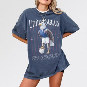 Vintage USMNT soccer fan graphic t-shirt with bald eagle soccer player and pinstripes on a faded navy graphic tee of USA world cup soccer fans