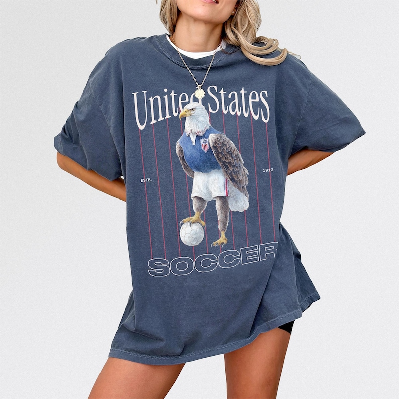 Vintage USMNT soccer fan graphic t-shirt with bald eagle soccer player and pinstripes on a faded navy graphic tee of USA world cup soccer fans