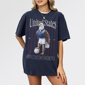 Vintage USMNT soccer fan graphic t-shirt with bald eagle soccer player on a navy comfort colors graphic tee of USA world cup soccer fans
