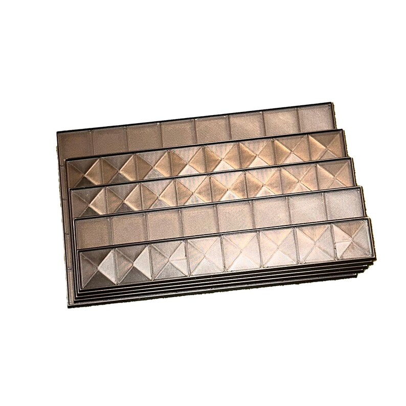 May include: A stack of rectangular, metallic-toned decorative tiles. Each tile features a grid pattern with diamond-shaped accents. The tiles are arranged in a layered fashion, showcasing their design and texture. The overall aesthetic is modern and geometric.