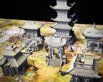 May include: A collection of gray miniature Asian-style buildings, including pagodas and temples, are arranged on a terrain mat. The structures feature detailed roof designs and architectural elements, suitable for tabletop gaming or model displays.