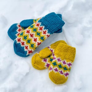 Könnte beinhalten: Zwei Paar Strickfäustlinge. Ein Paar ist blaugrün mit einem geometrischen Muster in Creme, Rot und Blaugrün sowie einem gerippten Bündchen. Das zweite Paar ist senfgelb mit einem geometrischen Muster in Creme, Blaugrün und Magenta.