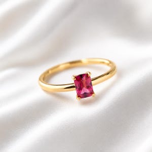 Minimalist pink ruby gemstone 925 sterling silver gold plated ring displayed on elegant white satin fabric with a softly blurred background.