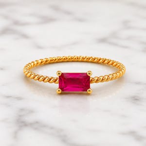925 Sterling Silver Gold Plated Ruby gemstone ring with twisted gold band displayed on soft white marble, focused closely on the jewelry.