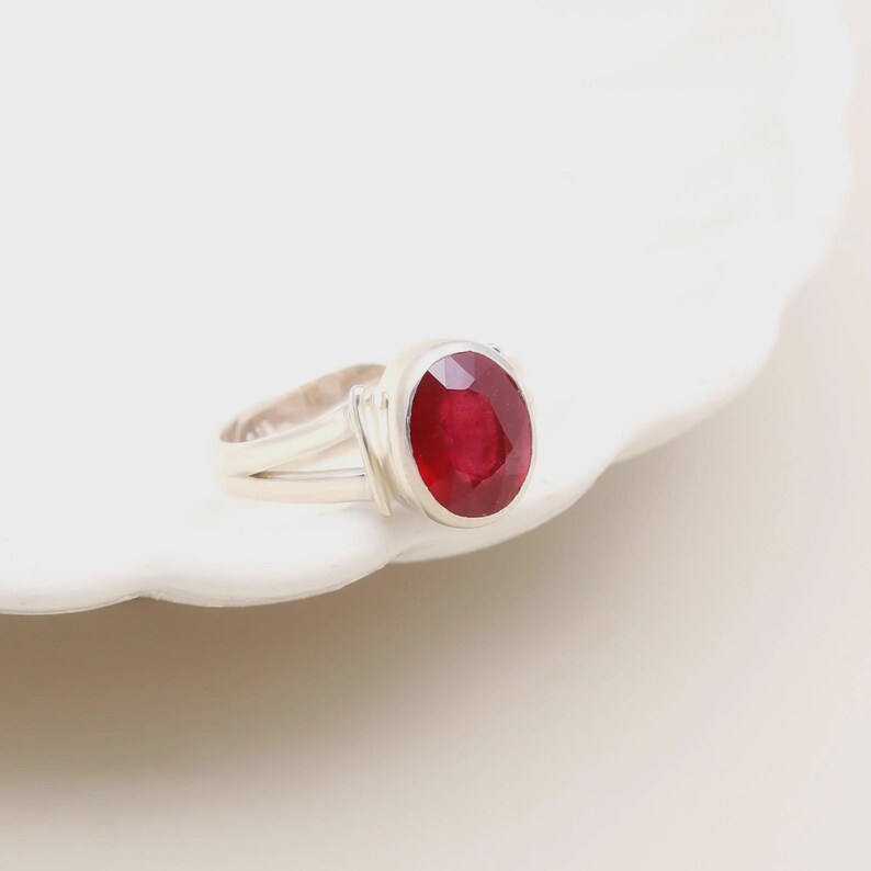 Op de afbeelding: Een zilveren ring met een grote, ovaal geslepen robijn. De robijn heeft een dieprode kleur en is gezet in een eenvoudige, elegante band. De ring wordt gepresenteerd op een wit oppervlak.