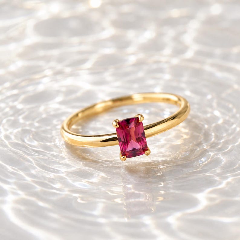 925 Sterling Silver Gold Plated Pink emerald ruby gemstone solitaire ring with polished gold band photographed on a bright white water ripple surface.