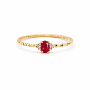 Può includere: Un anello in oro con una fascia a corda intrecciata. Il centro dell'anello è incastonato con un singolo rubino rosso taglio ovale, affiancato su ciascun lato da tre piccoli diamanti bianchi taglio rotondo e trasparenti in una montatura a griffe.