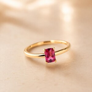 Dainty pink emerald ruby gemstone solitaire ring photographed on a warm champagne beige surface with soft lighting.
