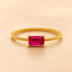 925 Sterling Silver Gold Plated Ruby statement ring with horizontal gemstone and twisted gold band on a warm champagne beige surface.