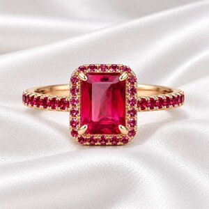 Emerald cut ruby statement ring with matching gemstone halo and 925 sterling silver gold plated band displayed on soft white satin.