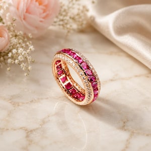 Peut inclure: Une bague en or rose composée d'une rangée centrale de pierres rondes rose vif, encadrée par deux rangées extérieures de petites pierres blanches transparentes. La bague présente une finition métallique polie et un design continu.