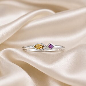 Può includere: Un anello in argento con due diverse pietre preziose in fila. Una pietra è un citrino giallo taglio marquise, l'altra è una pietra magenta più piccola a taglio quadrato. La fascia dell'anello è in argento lucido dal design pulito.