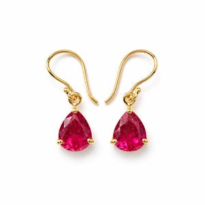 Könnte beinhalten: Ein Paar goldene Ohrhänger mit facettierten, birnenförmigen roten Edelsteinen. Jeder Ohrring hängt an einem einfachen Goldhaken, wobei der leuchtend rote Stein durch drei kleine Goldkrallen an der Basis der Fassung gehalten wird.