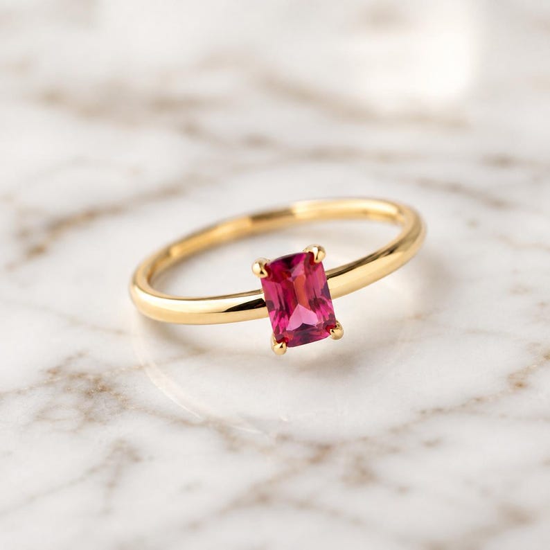Pink ruby gemstone 925 sterling silver gold plated solitaire ring displayed on a light marble surface, highlighting the stone and four-prong setting.