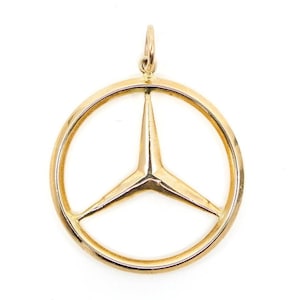 Può includere: Ciondolo dorato con il logo Mercedes-Benz, una stella a tre punte all'interno di un cerchio. Il ciondolo ha una finitura lucida e un piccolo anello per una catena. Il design è semplice ed elegante, adatto all'uso quotidiano.