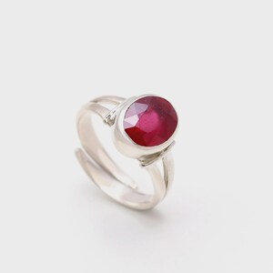 Op de afbeelding: Een zilveren ring met een grote, ovale robijn. De robijn is dieprood en gezet in een gepolijste zilveren band. De ring heeft een gespleten schachtontwerp. Een klassiek sieraad met een moderne twist.
