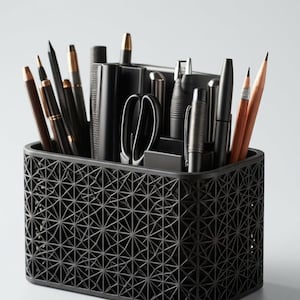 Puede incluir: Un organizador de escritorio rectangular de color negro con un patrón geométrico de celosía en sus paredes exteriores. El recipiente contiene varios instrumentos de escritura, incluyendo bolígrafos, lápices y unas tijeras, colocados verticalmente.