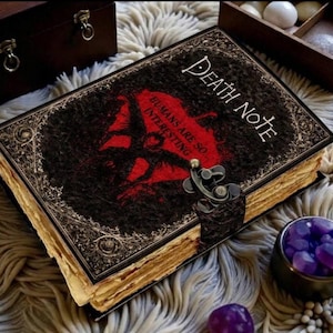 May include: A detailed, antique-style Death Note book with the title in white script. The cover is black with a red graphic and the text "Humans are so... interesting." The book has aged, yellowed pages and a metal clasp.