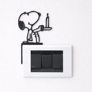 Peut inclure: Interrupteur Snoopy en métal noir tenant une bougie. Le couvercle est monté au-dessus d'une plaque d'interrupteur blanche avec trois interrupteurs noirs. Un ajout amusant et décoratif à n'importe quelle pièce.