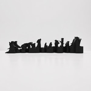 Può includere: Un oggetto decorativo nero con un design paesaggistico astratto. L'oggetto presenta una serie di picchi e valli, creando una silhouette di una catena montuosa o di un paesaggio urbano. L'oggetto è realizzato in un materiale nero opaco.