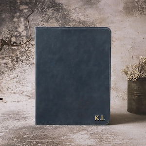 May include: A rectangular dark blue portfolio folder with rounded corners and visible stitching along the edges. The front cover features the gold embossed initials K.L in the bottom right corner, providing a personalised detail.