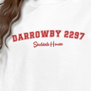 May include: White sweatshirt with the red text "DARROWBY 2297" arched across the chest, with "Skeldale House" below. The sweatshirt is a casual style, suitable for everyday wear.